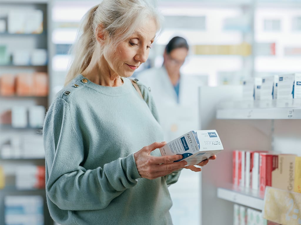 Pharmacy Drugstore: Portrait of a Beautiful Senior Woman Choosing to Buy Medicine, Drugs, Vitamins. Apothecary Full of Health Care Products, Supplement Bottles, Beauty Packages with Modern Design
